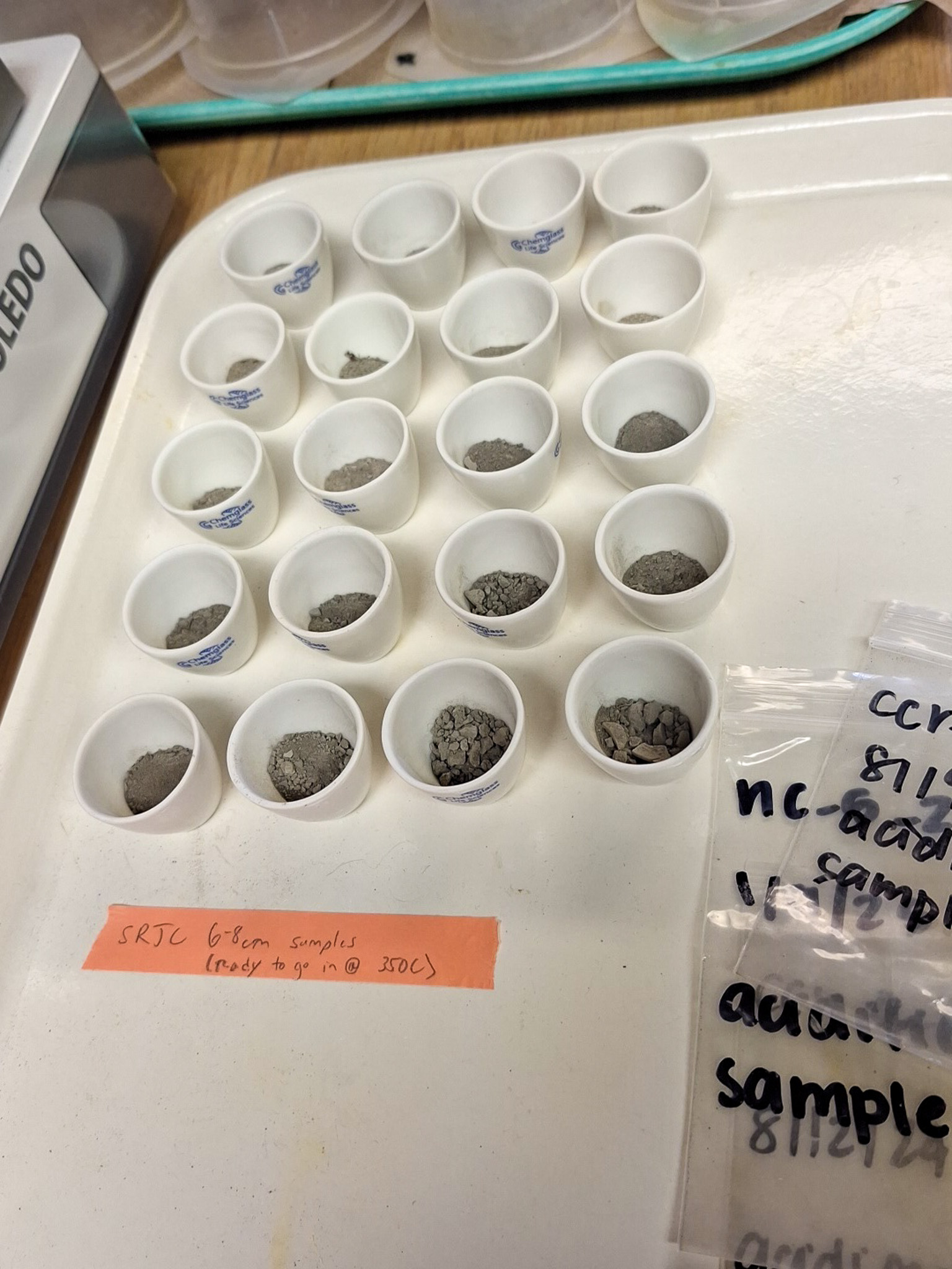 Lab tray of white sample cups with soil and rock fragments and handwritten labels