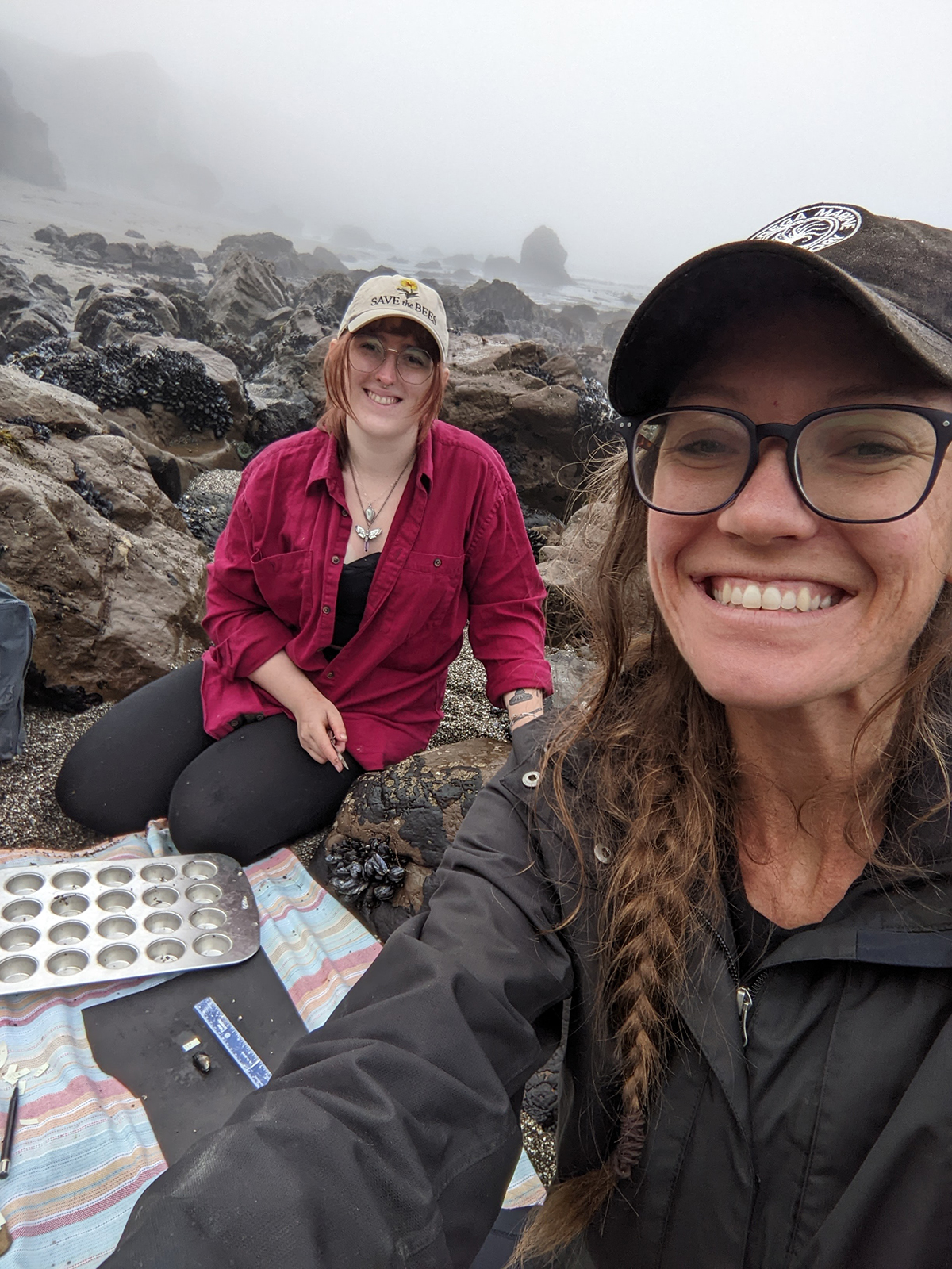 A selfie showing two people wearing jackets and hats in a foggy coastal setting