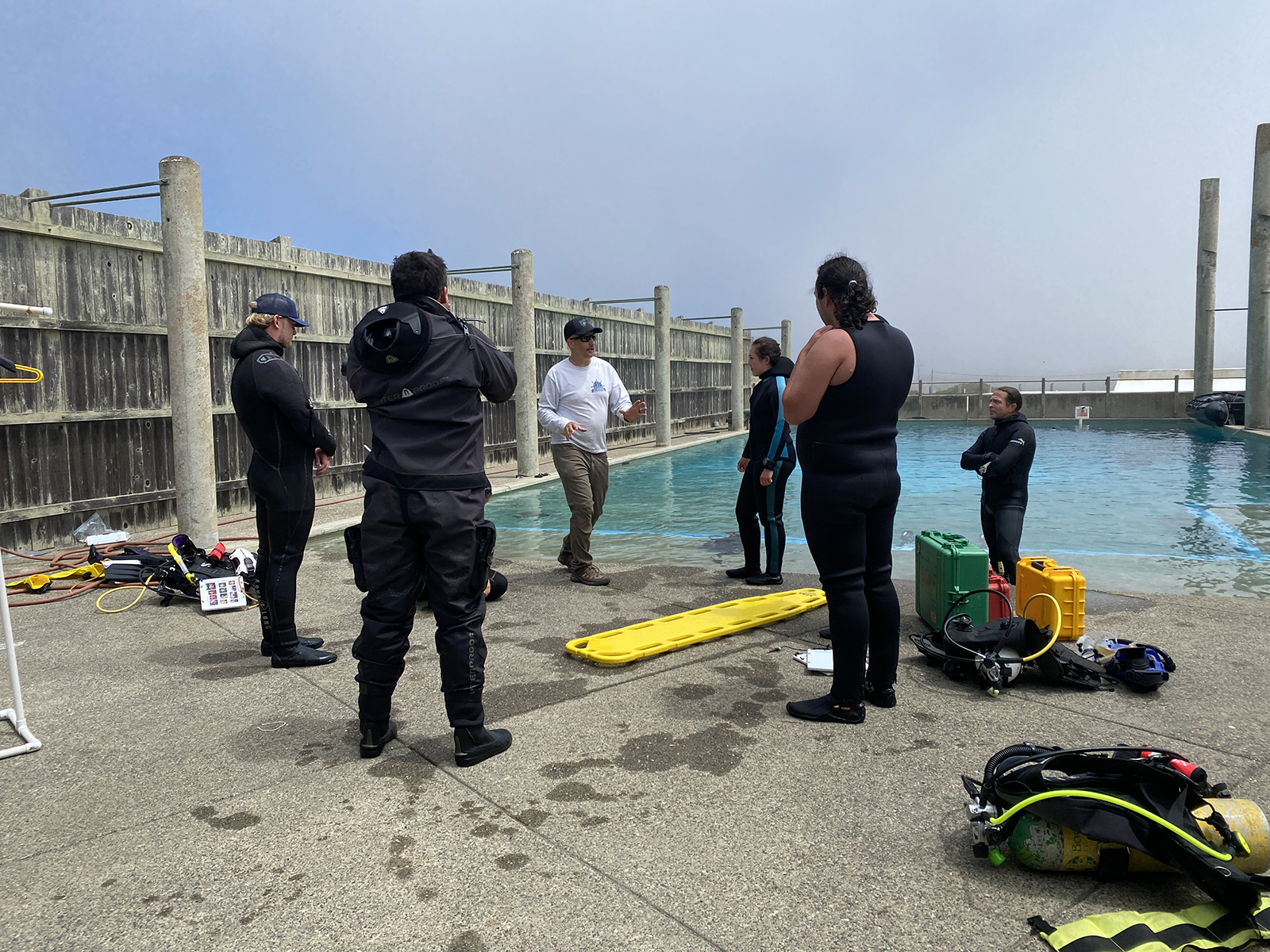 A group of people gathered around a training pool, listening to an instructor.