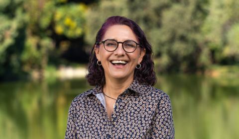 A portrait of Andrea Alfaro standing in front of greenery and joyfully laughing into the camera.
