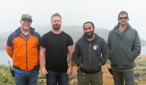 Four people standing in a row on a coastal bluff