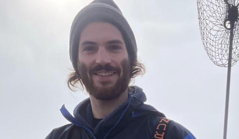 A portrait of Zeke Spooner wearing orange boating waders and holding a fish