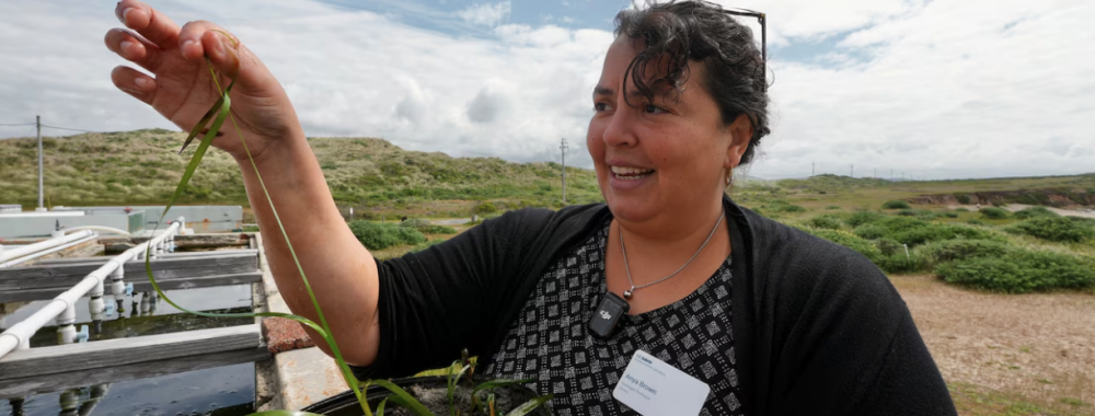 A portrait of Anya Brown standing next to a large tank of seagrass outside the Bodega Marine Laboratory