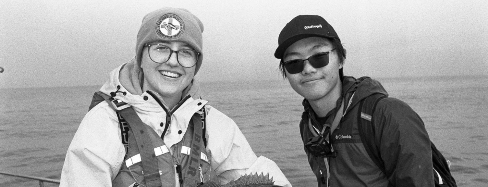 A black and white photo of SRJC Intern Alex Margand posing with another fisher, holding a large rockfish between them