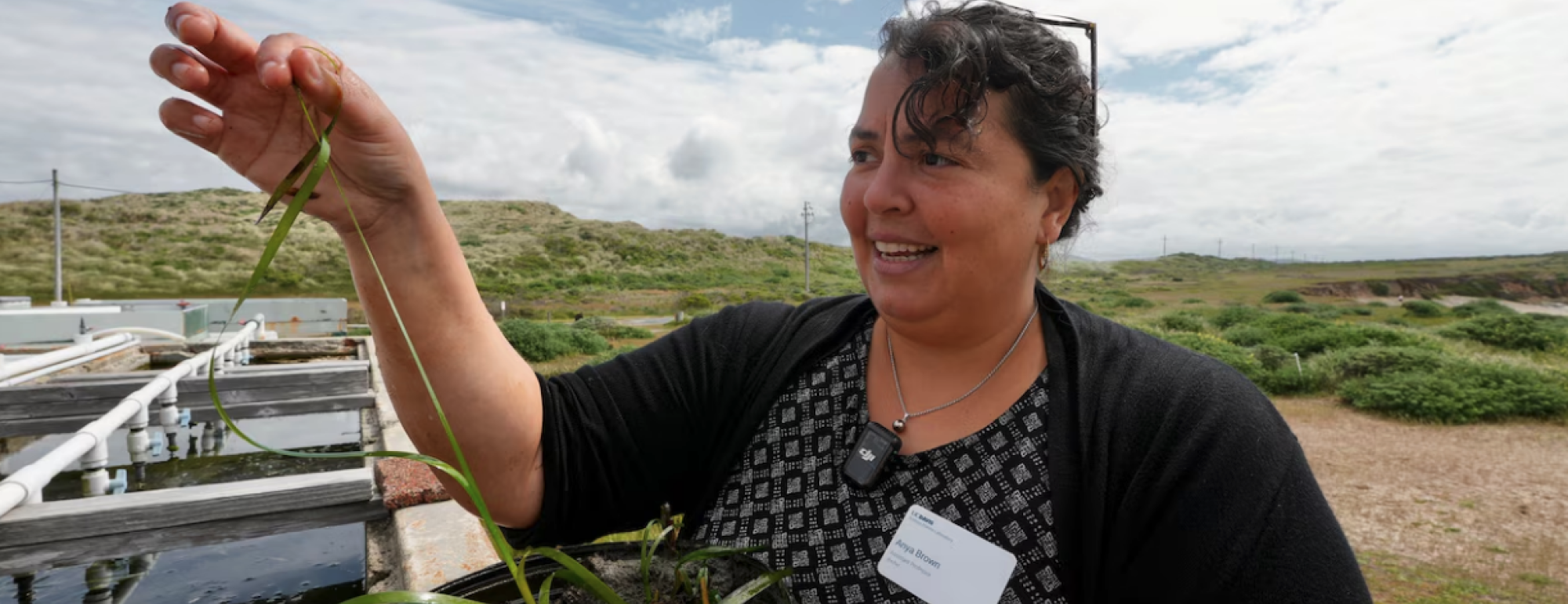 A portrait of Anya Brown standing next to a large tank of seagrass outside the Bodega Marine Laboratory
