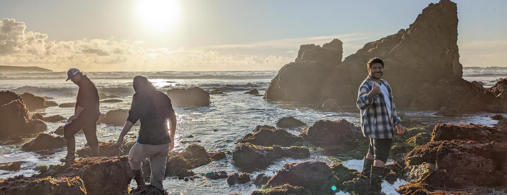 Three people balancing on partially submerged rocks with the sun rising behind them.