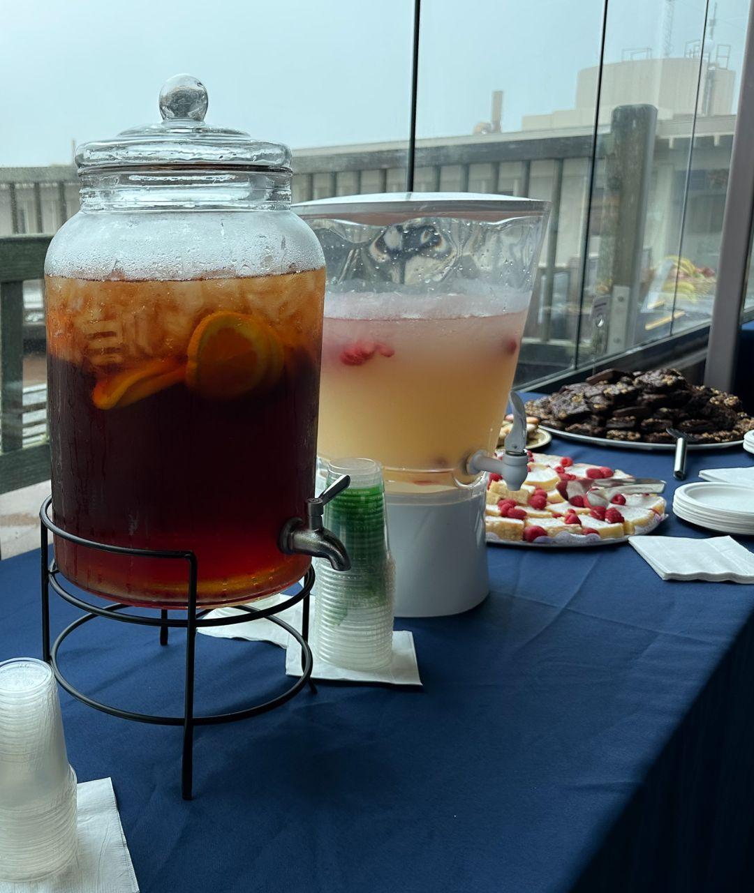 A beverage dispenser with iced tea set on a table with a blue tablecloth and other catering items on it