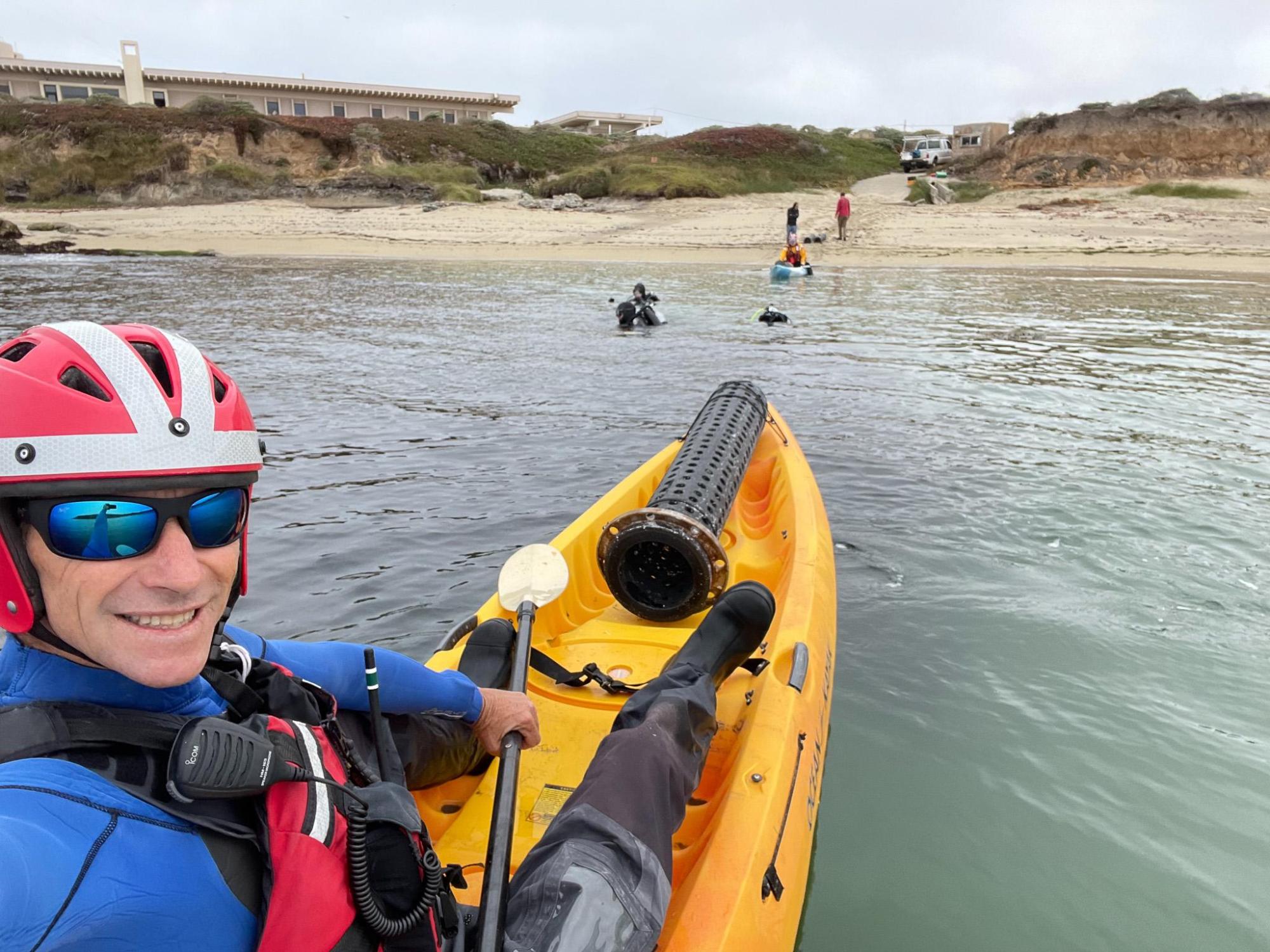 A person in a bright yellow kayak taking a "selfie" as the boat points towards the shore