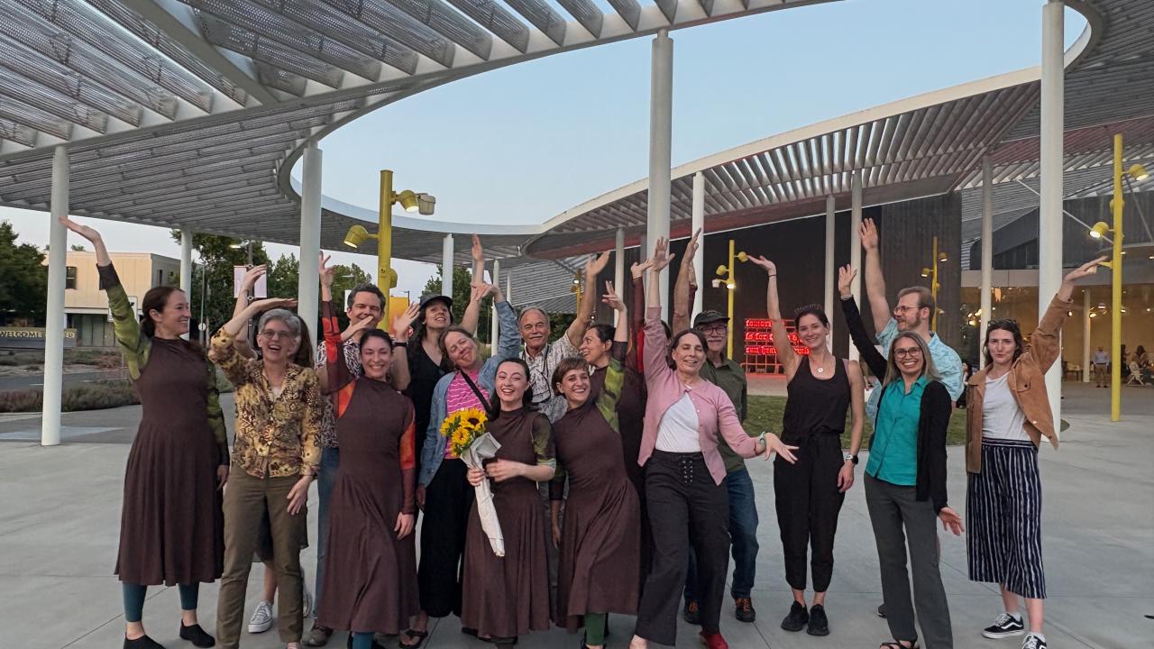 A large group of people posing for the camera under a metal structure outdoors