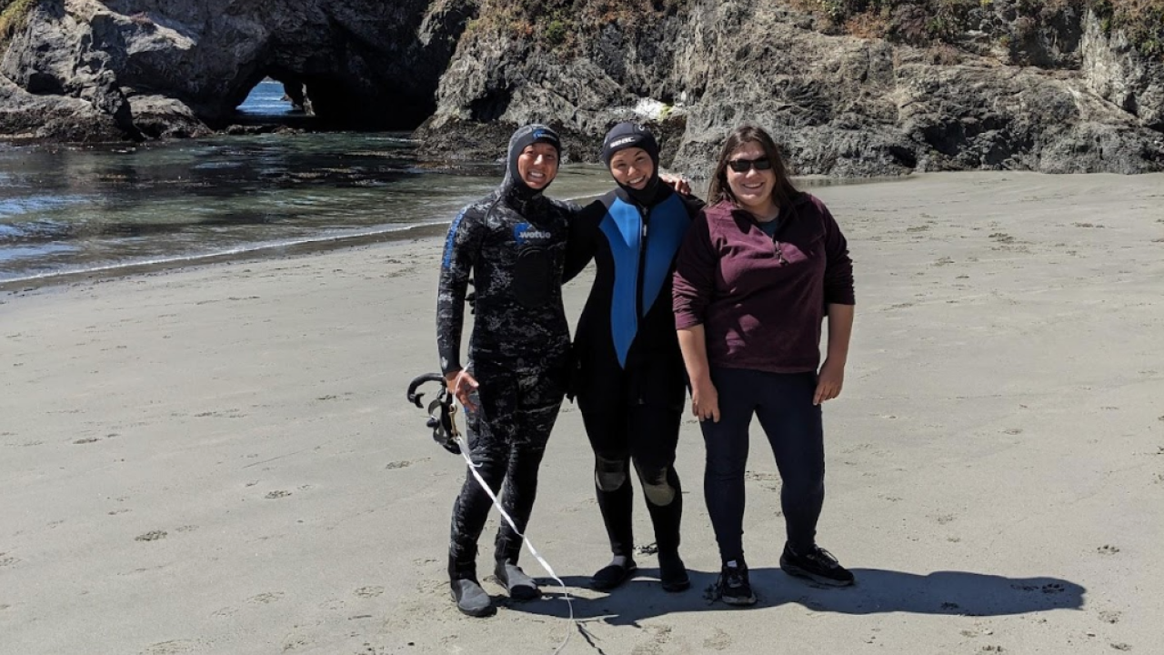 SRJC Intern Katherine Pearson posing with two people in dive gear on the beach