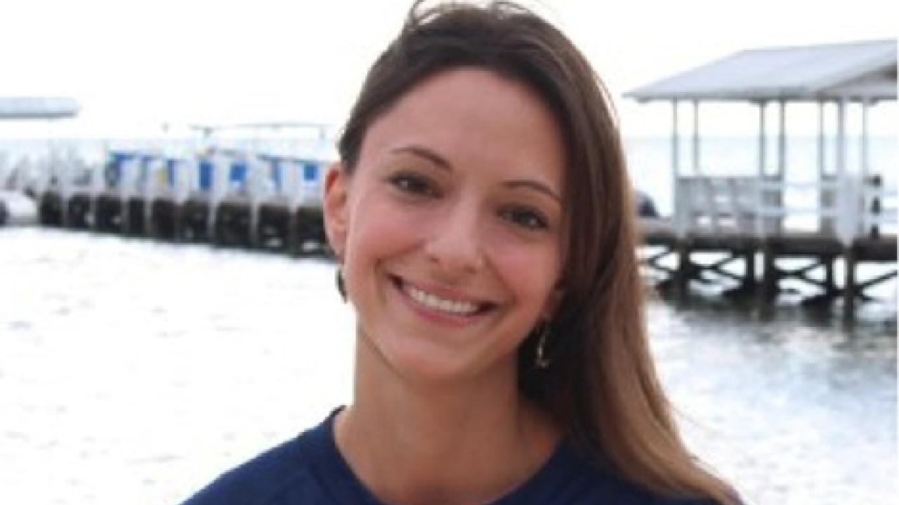 A person with long dark hair and a dark blue shirt standing in front of a boat dock.