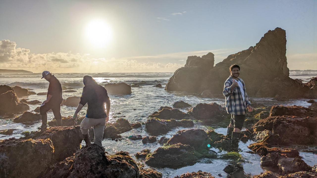 Three people balancing on partially submerged rocks with the sun rising behind them.