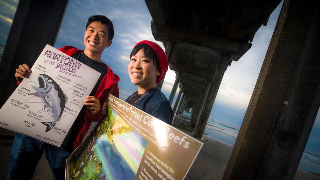 Two people holding up posters illustrating scientific information about marine creatures