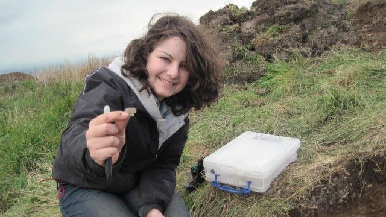 A person crouched down on a rocky landscape, holding up a small, organic object to the camera