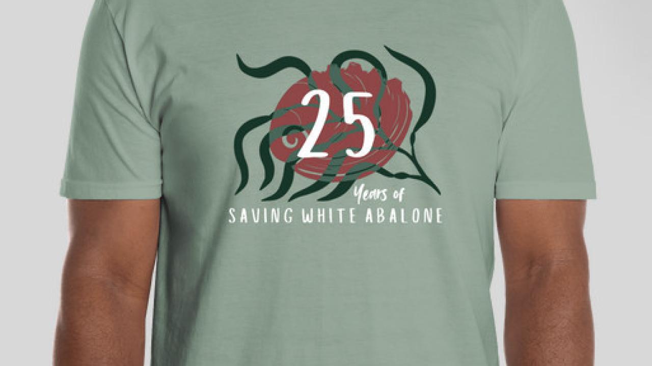 Person wearing sage-green T-shirt with '25 years of saving white abalone' text and stylized abalone and seaweed graphic