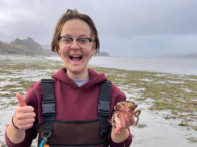 Leo Konefat looking excited and holding up a small crab while standing in a seagrass meadow