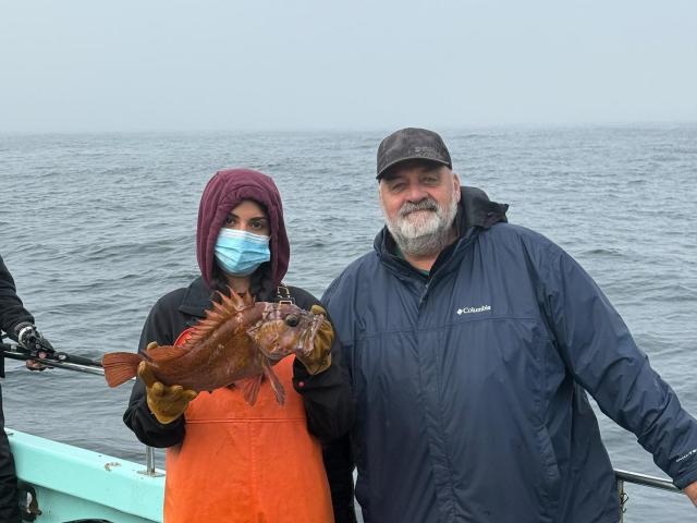 SRJC intern Esme Padilla-Garcia standing with another fisher on a boat, holding a fish caught as part of the CCFRP program