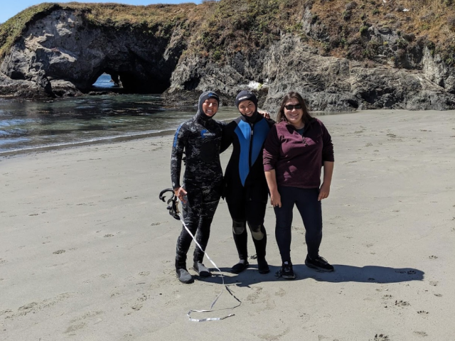 SRJC Intern Katherine Pearson posing with two people in dive gear on the beach