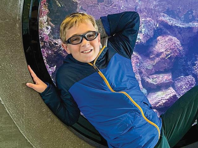 A photo of Matthew Gray leaning against the front of a circular tank filled with marine life in the Great Hall of Bodega Marine Laboratory