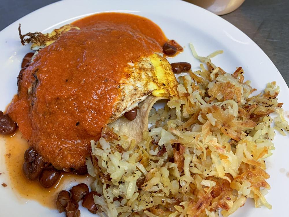 A close up of huevos rancheros on a plate with a side of hash browns
