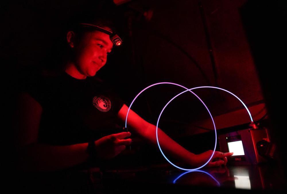 A researchers working in the dark on a piece of equipment with a swirl of tubing that glows brightly