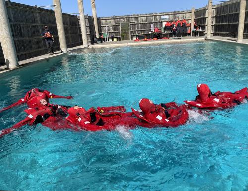 Several people in red survival suits floating in formation in a pool