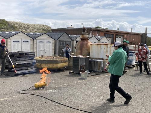 A person in a green shirt putting out a small fire with a fire extinguisher