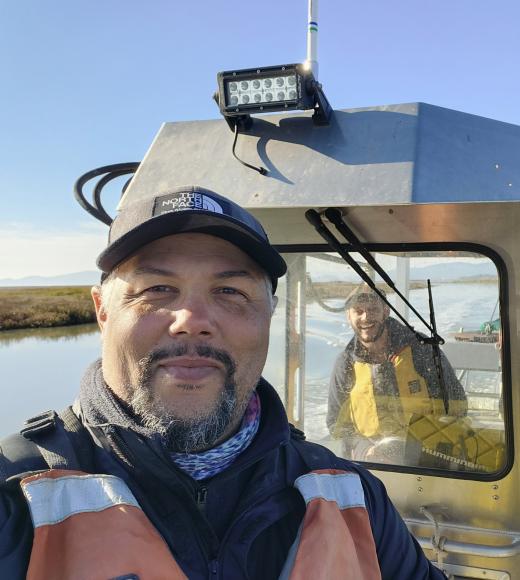 A portrait of Levi Lewis, wearing a life vest and standing on a boat in the water