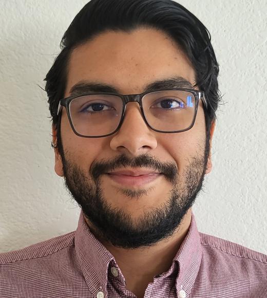 A portrait image of a person with short dark hair and a beard, glasses, and a button down shirt.