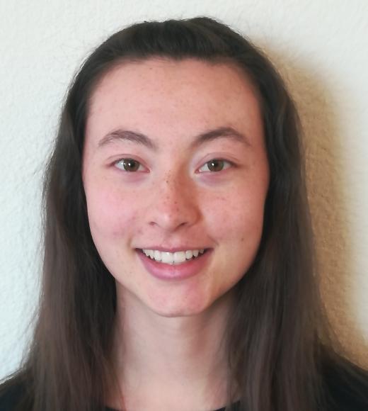 A profile image of a person with long dark hair standing in front of a white background.