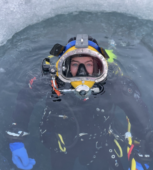 A person in dive gear mostly submerged in icy waters