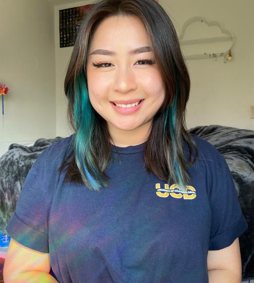 A person with shoulder length dark hair streaked with blue, wearing a navy UCD t shirt