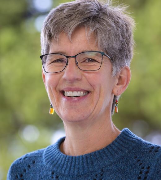 A profile image of a person with short hair and glasses, wearing a dark blue shirt and standing in front of a blurred background of greenery.