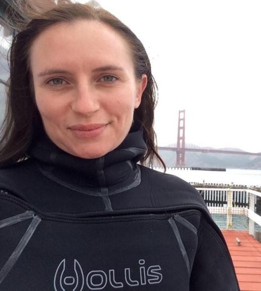 A person with long dark hair wearing a black scuba suit and standing on a boat