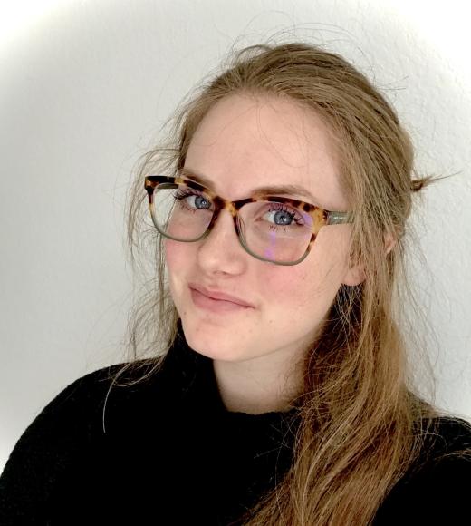 A person with long hair pulled back from their face and glasses looking at the camera
