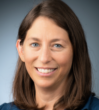 A close up portrait of a person with shoulder length brown hair against a gray background.