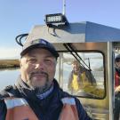 A portrait of Levi Lewis, wearing a life vest and standing on a boat in the water