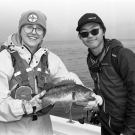 A black and white photo of SRJC Intern Alex Margand posing with another fisher, holding a large rockfish between them