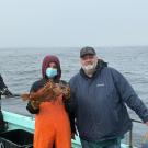 SRJC intern Esme Padilla-Garcia standing with another fisher on a boat, holding a fish caught as part of the CCFRP program