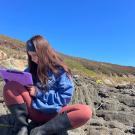 A person sitting on a rocky coastal area, making notes in a notebook