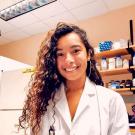 A person with long curly hair in a while lab coat, smiling at the camera
