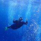 A full-body shot of Anya Brown snorkeling. She raises her hands up as bubbles swirl around her. 