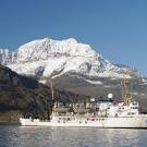 NOAA Ship on the water with a snowy mountain behind it.