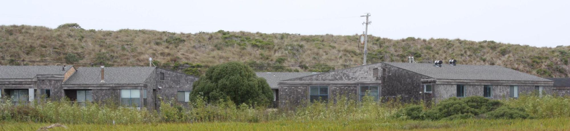 A panoramic view of housing at Bodega Marine Laboratory, showing buildings covered in rustic wood siding and surrounded by coastal prairie.